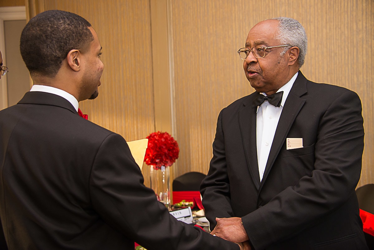 Two brothers in formal attire shaking hands at gala dinner